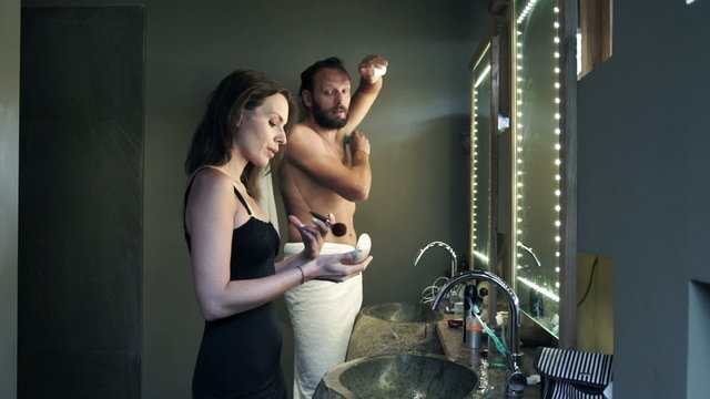 Young couple in bathroom, woman applying makeup and man antiperspirant
