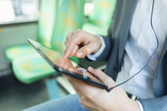 Man listening music with tablet pc in a bus texting message. Close up