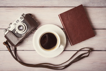 Vintage camera, notebook and cup of coffee over wooden desk