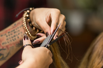 Closeup stylist hands with tattoo cutting brunette hair using