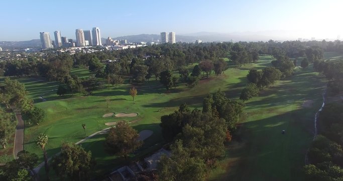 Shadows and sunlight across golf course lifting raising aerial above view flyby trees park