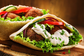 Falafel and fresh vegetables in pita bread on wooden table - obrazy, fototapety, plakaty