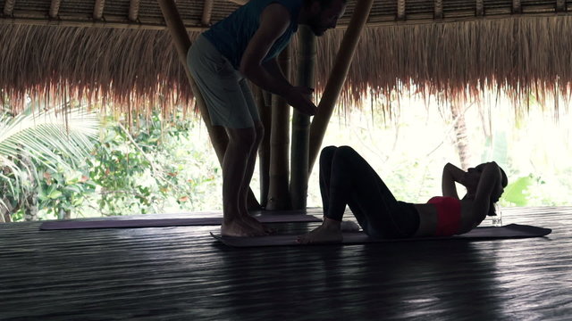 Young woman doing crunches in wooden barn with personal trainer
