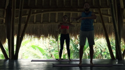 Young couple doing waist twist exercise in wooden barn 
