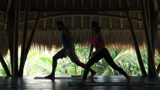 Young couple exercising yoga, doing warrior pose in wooden barn

