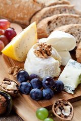 Cheese platter: variety of cheeses on wooden plate with fruits and bread
