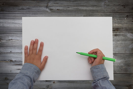 Child Holding Pen On Blank Sheet Of Paper. Kid Draws On White Paper.