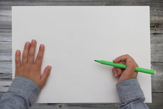 child holding pen on blank sheet of paper. kid draws on white paper.