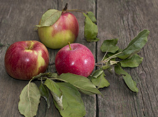 three apples with leaves on a wooden table