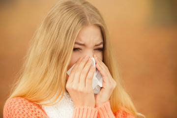 Sick ill woman in autumn park sneezing in tissue.