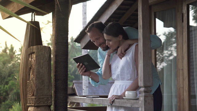 Young couple talking over tablet computer while standing on terrace
