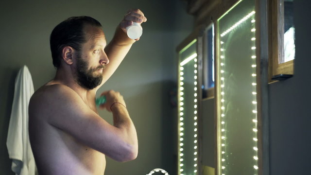Young man in towel applying antiperspirant on his armpit in bathroom