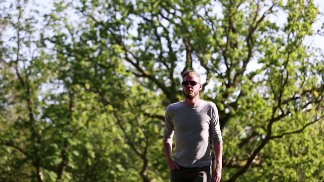 A handsome man walking along a path going up on a sunny summer day. Hand held video from a low angle.
