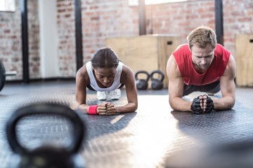 Muscular couple doing planking exercises