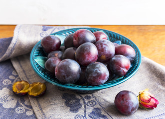 Purple plums in a green plate on a wooden table