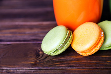 Close view at orange and green french pistachios and orange macaroons in dark colors on a wooden background. Shallow depth of field. Focus at first macaroon.