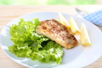Dish of fish fillet with lettuce and lemon on table close up