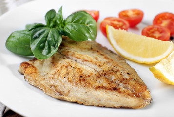 Dish of fish fillet with basil and lemon on plate close up