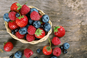 Sweet tasty berries in basket on wooden table close up