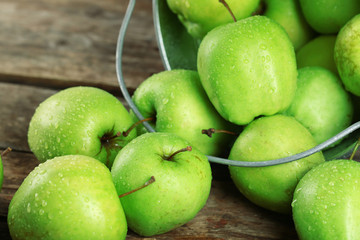 Ripe green apple in metal bucket on wooden table close up