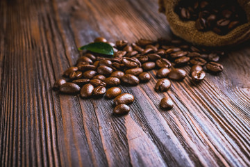 Coffee beans with leaf on wooden table close up