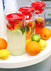 Full jugs with drinks and fruits on table close up
