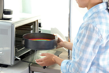 Young woman making rainbow cake in kitchen