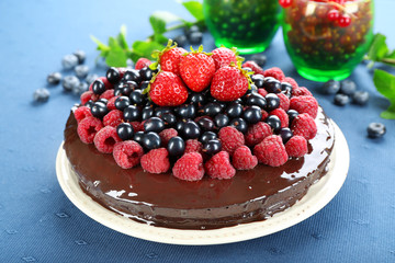 Delicious chocolate cake with summer berries on blue tablecloth background