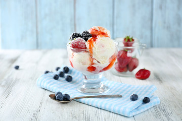 Delicious ice cream with fresh frozen berries and sauce, on color wooden background