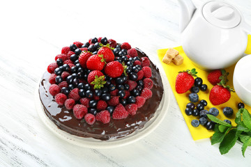 Delicious chocolate cake with summer berries on white wooden background