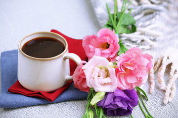 Cup of coffee with flowers near books on sofa in room