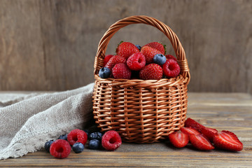 Tasty ripe berries in basket on wooden table close up