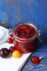 Tasty homemade plum jam in glass jar on wooden background