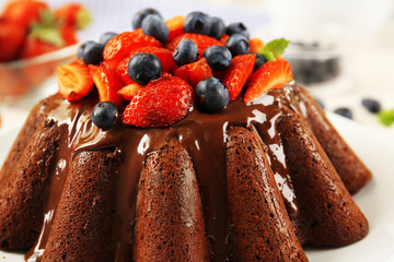 Tasty chocolate muffin with glaze and berries on table close up