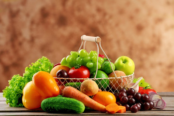 Heap of fresh fruits and vegetables in basket on wooden table close up