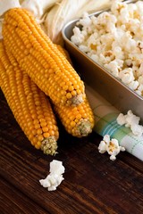 Three corncobs next to pan with fresh popcorn