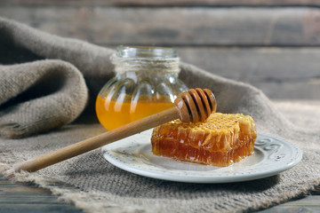 Pot of honey and honeycomb with dipper on wooden table