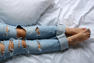 Woman in blue jeans on bed top view