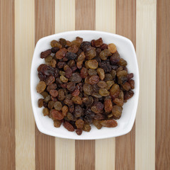 Raisins served in white plate on a wooden table. Photo taken from above.