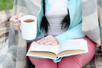 Young woman with book sitting on green grass outdoors