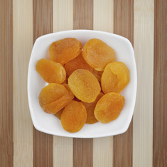 Dried apricots served in white plate on a wooden table. Photo taken from above. 
