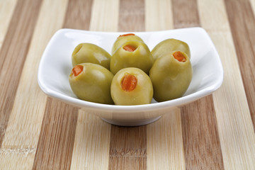 Green olives in white plate on wooden table. Studio shot. Selective focus.