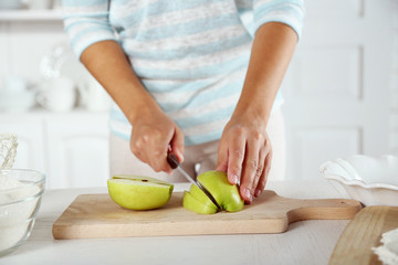 Female hands slicing apple for pie, close-up, on light background