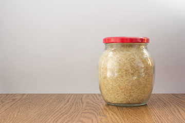 Full glass jar with rice closed red cap on wooden table