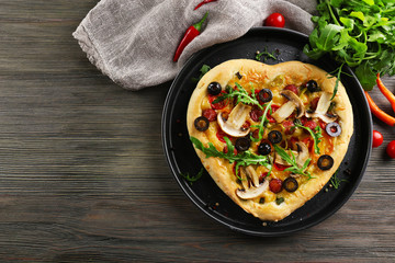 Heart shaped pizza on metal tray on wooden background