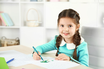 Cute little girl doing her homework, close-up, on home interior background