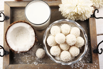Homemade sweets in coconut flakes and fresh coconut on tray, close-up