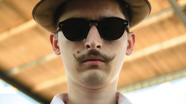 man with a mustache wearing sunglasses and a hat watching you