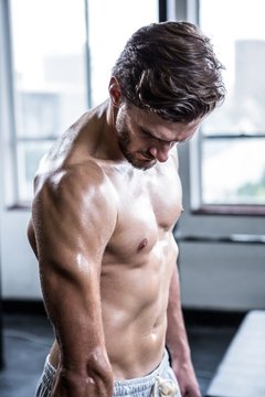 Shirtless man flexing his bicep while standing in gym