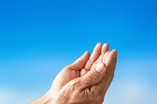 Two open empty hands of old woman with sky background